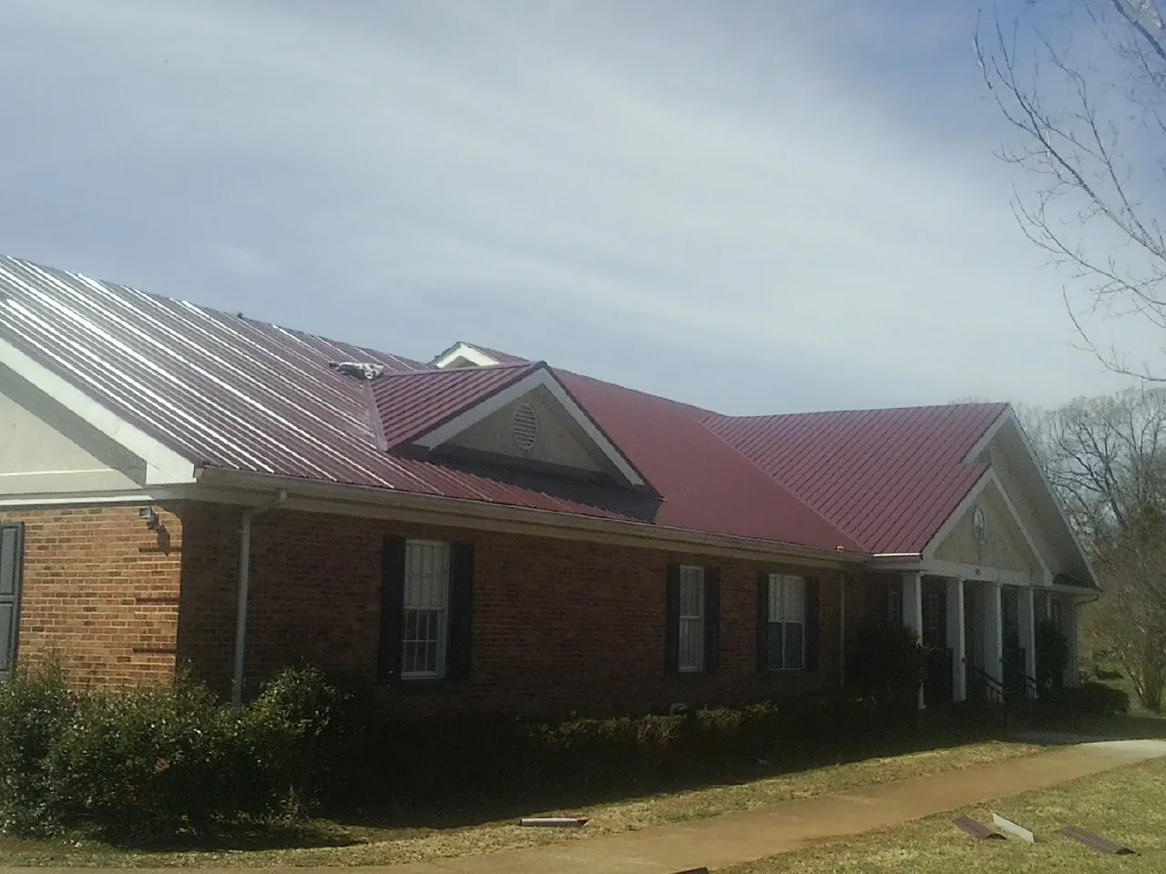 Red metal roof with gabled entries on a long brick building, from a Hail Damage Roof Repair job in Millheim