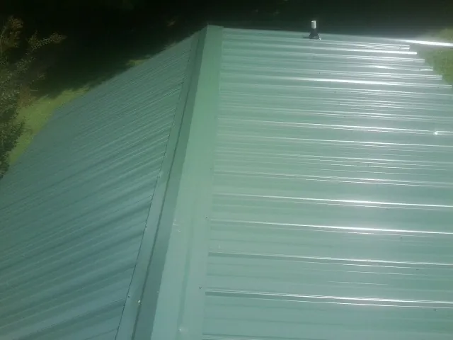 New green metal panels meeting at the ridge of a roof — Flat Roof Repair work by our crew in Millheim