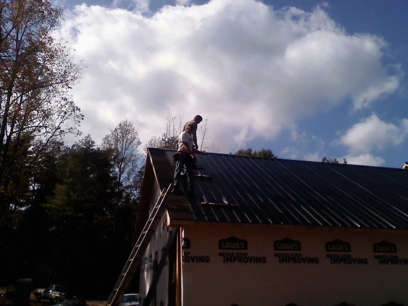 Roofer fastening dark metal panels high against a cloudy sky, from a Roof Inspection job in Millheim