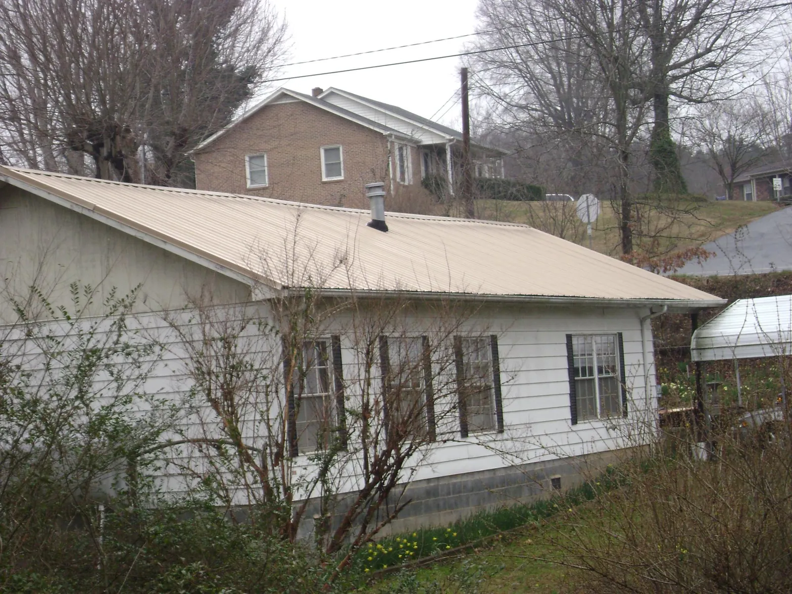 Tan metal roof on a white sided house set into a hillside — Commercial Roofing by Roofing Brothers in Millheim